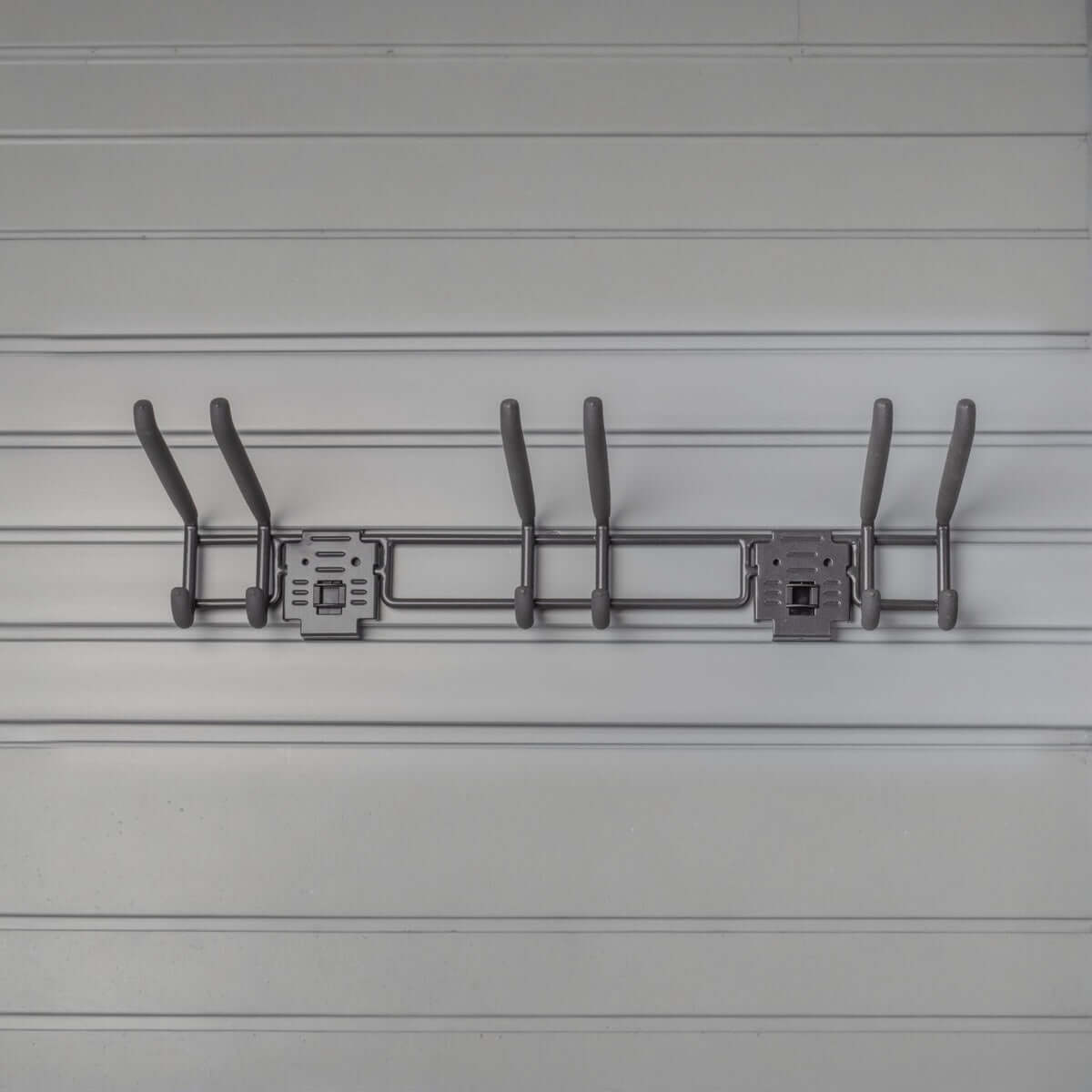 Slatwall hooks on a 24" tool bar mounted to gray slatwall panels, holding garden and garage tools organized neatly