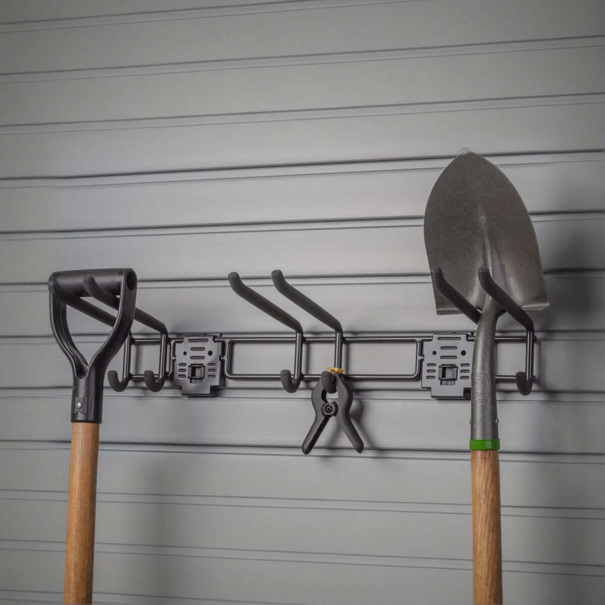 Slatwall hooks on a 24" tool bar organizing garden tools including shovels and pruners on a gray slatwall panel