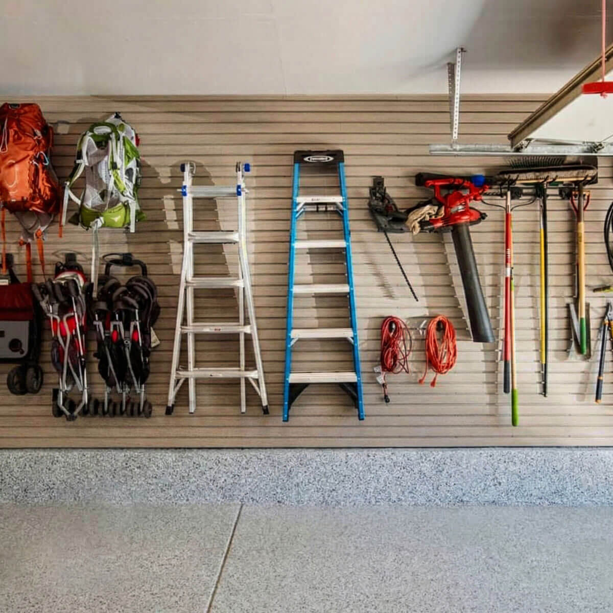 Slatwall Panels organizing a garage wall with ladders, backpacks, garden tools, leaf blower, and extension cords__Beachwood