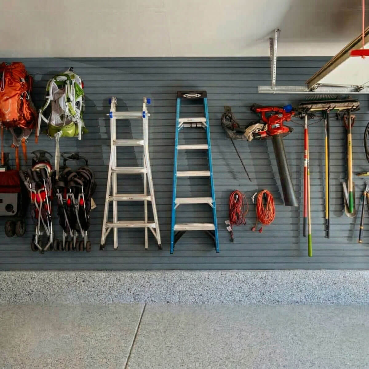 Slatwall Panels organizing a garage wall with ladders, backpacks, power tools, extension cords, and garden tools__DriftwoodSlate