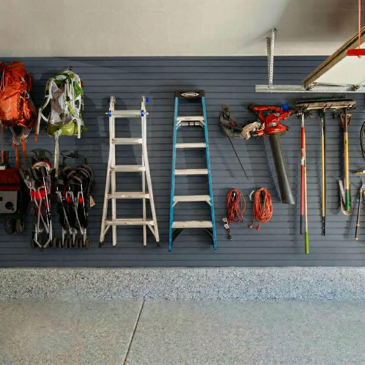 Slatwall Panels organizing a garage wall with ladders, backpacks, power tools, extension cords, and garden tools__Graphite