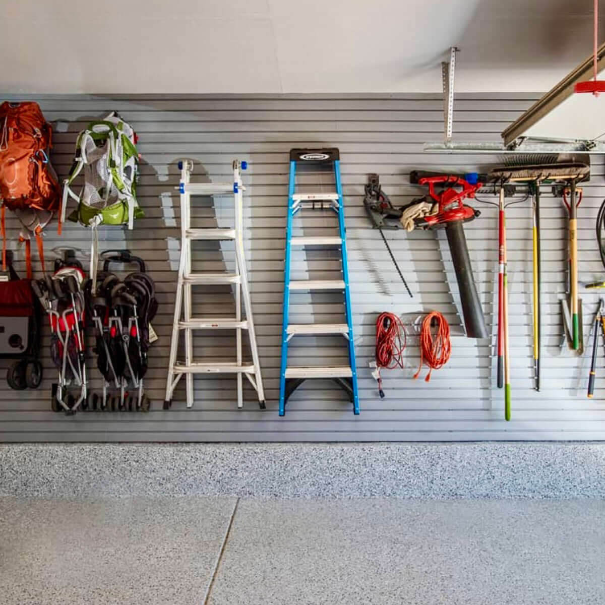 Slatwall Panels organizing a garage wall with ladders, backpacks, garden tools, leaf blower, and extension cords neatly displayed.__Gray