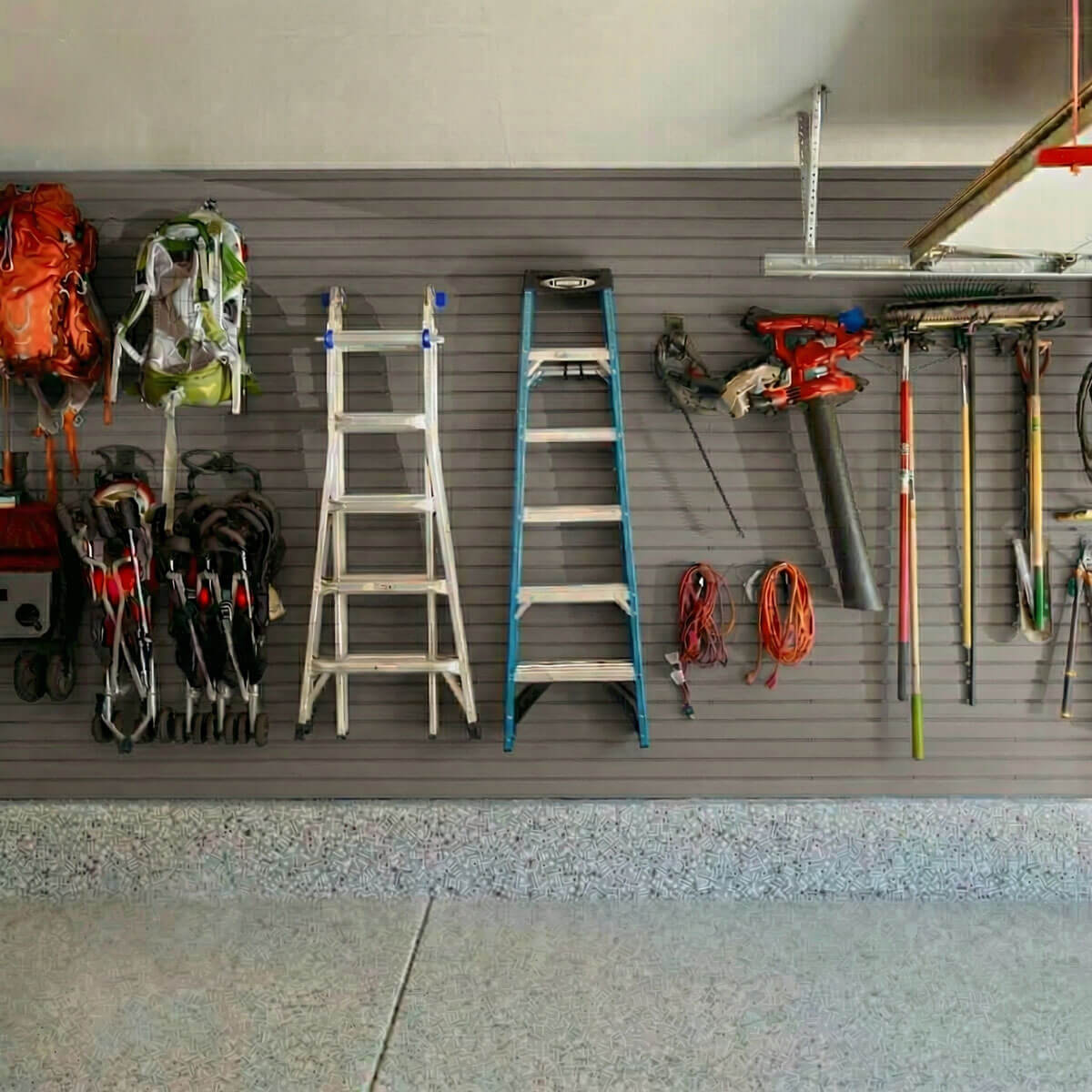 Slatwall Panels organizing a garage wall with ladders, backpacks, power tools, extension cords, and long-handled yard tools__Taupe